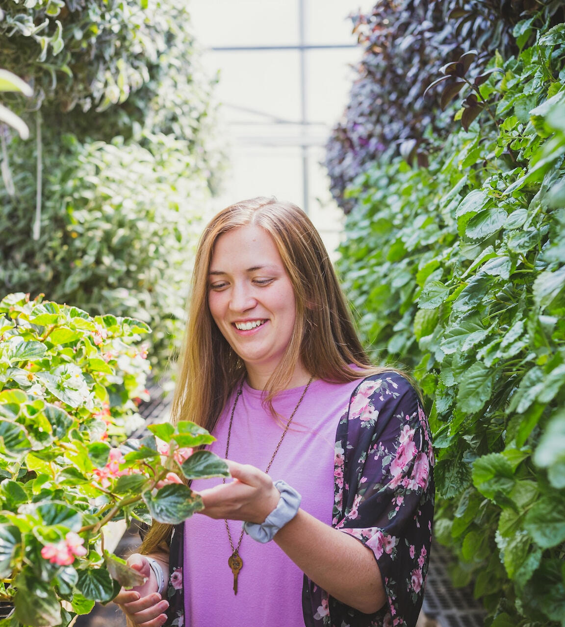 Woman standing in a greenhouse looking at leaves and smiling